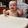 baby, high_chair, kitchen, refrigerator, magnet, photo, note, cabinet, countertop, smiling, child, food_tray, arm, face, furniture, indoor, person, expression, table, cute