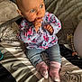 baby, child, blue_eyes, floral_clothing, pink_socks, bed, blanket, patterned_bedspread, indoor, cute, person, infant, sitting, hand_near_mouth, curious, soft_lighting, portrait, casual, home, cozy