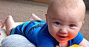 Abel is registered to the contest to win money with this photo: baby, blue_clothing, carpet, child, colorful, cute, face, floor, happy, indoor, infant, person, pillow, play_mat, playtime, smiling, soft_book, toddler, toy, young_child