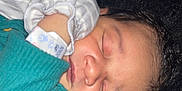 Masai is registered to the contest to win money with this photo: newborn, baby, sleeping, face, hand, mitten, curly_hair, skin, closeup, peaceful, resting, clothing, infant, portrait, young_child, soft_lighting, cute, tiny, healthcare_bracelet, comfort
