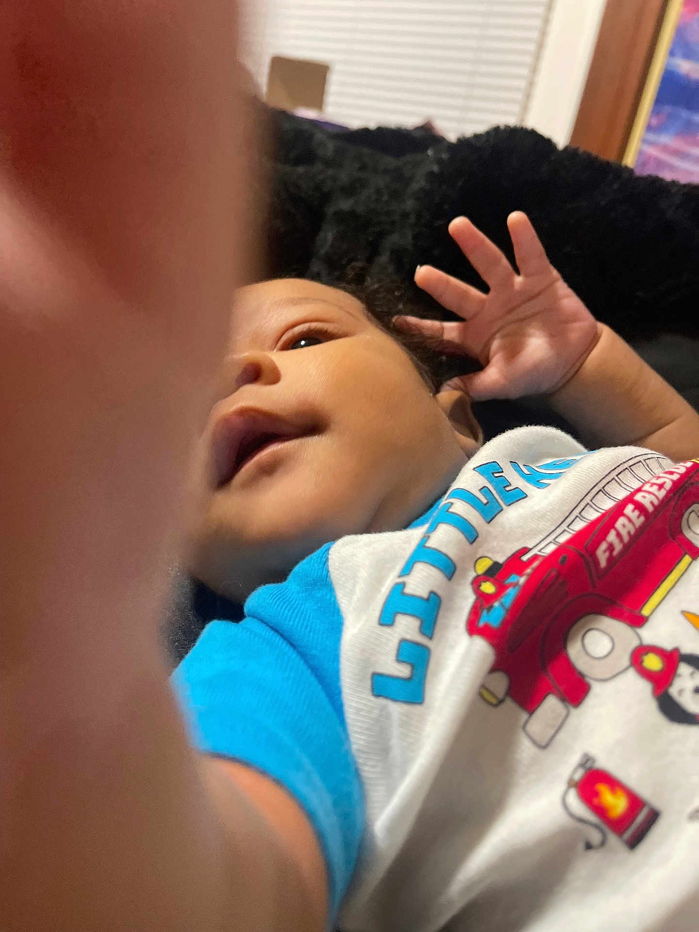 Masai joined the competition — help win amazing prizes! baby, infant, child, hand, face, shirt, clothing, text, fire_truck, toy, furniture, blanket, indoor, cozy, curious, close_up, portrait, person, smile, baby_garment
