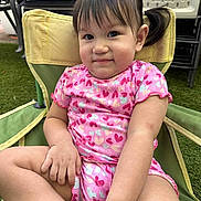 Angelina is registered to the contest to win money with this photo: toddler, child, smiling, pink_clothing, heart_pattern, chair, outdoor, grass, short_hair, pigtails, cute, sitting, happy, young_child, casual, daylight, skin, person, relaxed, summer