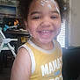 toddler, child, smiling, yellow_shirt, cream_on_face, cream_on_arm, indoor, high_chair, furniture, happy, person, portrait, curly_hair, playful, closeup, casual_clothing, home, daylight, expression, cute