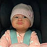 baby, child, car_seat, pink_hat, pajamas, infant, seatbelt, face, expression, indoors, cushion, safety, clothing, headwear, warning_label, pout, person, cute, infancy, car_interior