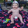 baby, child, outdoor, blanket, diaper, hat, toy, smile, happy, sitting, floor, pavement, colorful, person, cushion, furniture, nature, greenery, daylight, playtime