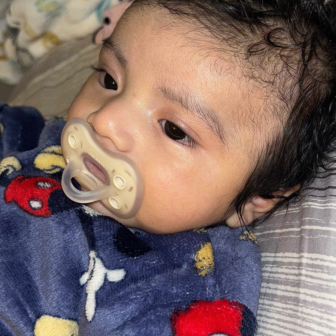 Ian is registered to the contest to win money with this photo: baby, bed, blanket, child, close_up, comfort, cozy, curly_hair, cute, face, head, indoors, infant, mickey_mouse, pacifier, resting, sleepwear, soft_texture, striped_bedspread, young_child