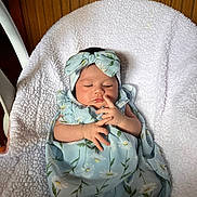 Ricah Olivia is registered to the contest to win money with this photo: baby, infant, sleeping, blanket, headband, floral_pattern, blue_clothing, white_blanket, wooden_background, peaceful, newborn, child, resting, cute, soft_texture, indoors, portrait, person, wrapped, comfort