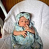 baby, infant, sleeping, blanket, headband, floral_pattern, blue_clothing, white_blanket, wooden_background, peaceful, newborn, child, resting, cute, soft_texture, indoors, portrait, person, wrapped, comfort