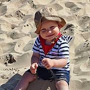 Louka a rejoint le concours — aidez-le/la à gagner de superbes lots ! barefoot, beach, casual_clothing, child, cute, daylight, happy, hat, nature, outdoor, playing, sand, sitting, smiling, striped_shirt, summer, sunlight, toddler, vacation, young_child