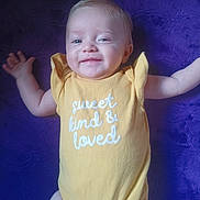 Lainey is registered to the contest to win money with this photo: baby, smiling, yellow_onesie, purple_blanket, infant, happy, face, arms, cute, child, lying_down, text_on_clothing, portrait, skin, one_person, indoors, young_child, soft_texture, fabric, human