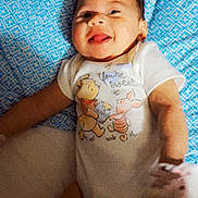 Hazel is registered to the contest to win money with this photo: baby, infant, child, smiling, tongue_out, lying_down, portrait, indoor, blanket, blue_blanket, onesie, clothing, storybook_characters, winnie_the_pooh, tigger, adult_hands, cozy, happy, face, bed