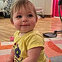 Allie is registered to the contest to win money with this photo: baby, child, toddler, sitting, yellow_shirt, pink_shorts, carpet, crib, floor, indoor, smile, happy, person, furniture, book, toy, wooden_floor, colorful, room, curtains