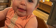 Allie joined the competition — help win amazing prizes! baby, child, high_chair, wooden_furniture, indoor, person, cute, smiling, table, hand, hair, pigtails, clothing, store, background, blur, face, eyes, skin, infant