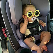 Allie is registered to the contest to win money with this photo: baby, car_seat, pacifier, sunglasses, child, infant, car_interior, seatbelt, purple, cute, small_hair_tie, foot, hand, toy, cup_holder, sunlight, casual, comfort, child_safety, car
