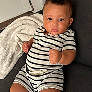 Carter is registered to the contest to win money with this photo: baby, child, curly_hair, striped_clothing, couch, blanket, indoors, portrait, person, furniture, cute, infant, expression, raised_fists, seated, cozy, soft_texture, casual, young, looking_at_camera