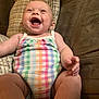 Lakelynn is registered to the contest to win money with this photo: baby, laughing, onesie, colorful_clothing, couch, pillow, happy, infant, child, smiling, seated, indoors, furniture, cute, skin, person, young_child, cheerful, plaid_pattern, relaxed