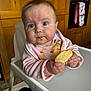 Penelope joined the competition — help win amazing prizes! baby, child, high_chair, cookie, bib, pink_clothing, messy, kitchen, wooden_cabinets, curious_expression, indoor, person, face, hands, food, table, appliance, toddler, cute, seated