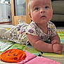 Penelope joined the competition — help win amazing prizes! baby, infant, child, play_mat, toy, soft_toy, orange_toy, cherry_toy, floral_onesie, curious_expression, indoor, carpet, colorful, couch, furniture, face, hands, legs, floor, head