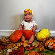 Penelope is registered to the contest to win money with this photo: baby, child, pumpkin, yellow_bow, autumn_leaves, fall, carpet, white_wall, cute, smiling, orange_pumpkin, white_pumpkin, decor, indoors, seasonal, holiday, festive, happy, sitting, headband