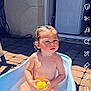 baby, bath_time, bathtub, child, curious_expression, daylight, door, outdoor, pavement, person, playful, rubber_duck, skin, soap_suds, summer, sunlight, toddler, toy, water, wet_hair