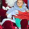 baby, child, santa_claus, holiday, christmas, red_background, costume, beard, glasses, colorful_clothing, smiling, festive, indoor, person, seated, blanket, boots, fur_trim, portrait, cute