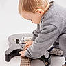 toddler, child, guitar, electric_guitar, musical_instrument, gray_clothing, knitwear, indoor, footwear, slippers, baby, music, playing, curious, young_child, studio, white_background, portrait, exploration, hands