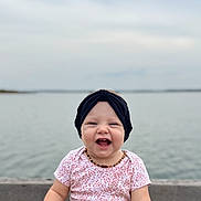 Makenzie joined the competition — help win amazing prizes! baby, smiling, child, headband, denim, water, lake, outdoor, happy, sitting, infant, toddler, casual_clothing, nature, sky, cloudy, portrait, cute, joyful, accessory