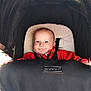 baby, stroller, infant, child, smiling, face, black_canopy, red_clothing, seatbelt, happy, person, portrait, baby_carrier, cute, indoors, head, young_child, comfort, transportation, closeup
