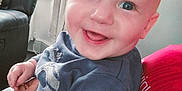 Harrison is registered to the contest to win money with this photo: baby, child, smiling, indoor, person, blue_eyes, sweater, hand, couch, curtain, window, living_room, red_clothing, decor, heart_shape, happy, face, seated, closeup, human