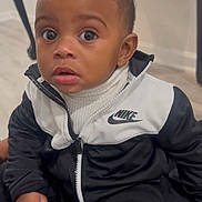 Jacolby is registered to the contest to win money with this photo: child, toddler, indoor, nike, jacket, curious, wide_eyes, face, person, clothing, table, wood, floor, expression, portrait, casual, sitting, young_child, cute, fashion