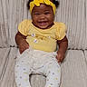 baby, child, infant, smiling, portrait, yellow_outfit, headband, bow, butterflies, leggings, shoes, seated, quilted_background, indoor, close_up, happy, fashion, baby_clothing, dark_skin, adorable