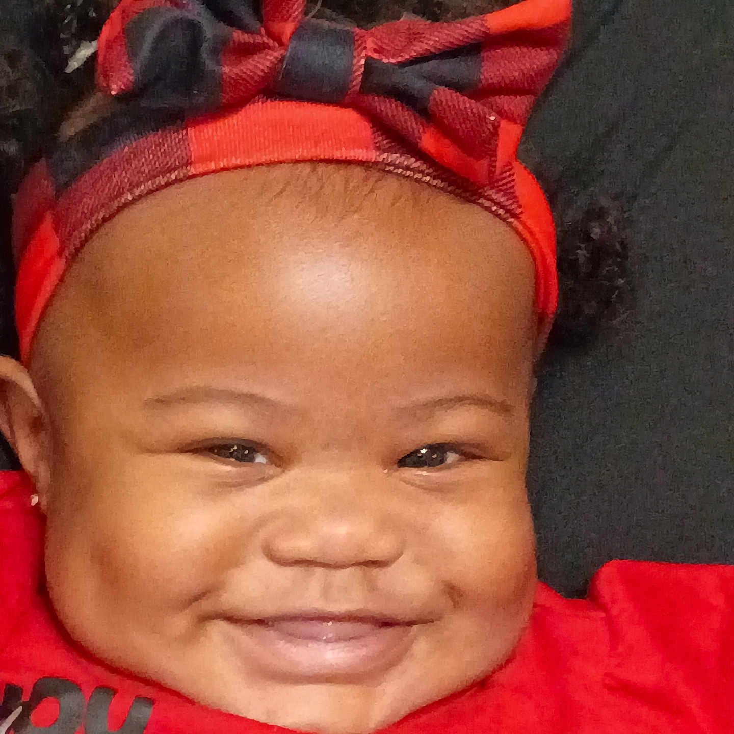 Blessing is registered to the contest to win money with this photo: baby, infant, child, portrait, smiling, happy, face, head, red_outfit, hair_bow, bow, headband, close_up, indoor, seated, looking_at_camera, black_background, fashion, cute, photography