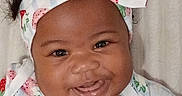 Blessing is registered to the contest to win money with this photo: baby, black_hair, blanket, bow, brown_skin, child, close_up, curly_hair, dress, fabric, face, happy, headband, indoors, infant, patterned_clothing, photography, portrait, smiling, strawberry