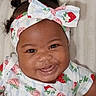 Blessing is registered to the contest to win money with this photo: baby, infant, child, smiling, portrait, close_up, face, headband, bow, strawberry, patterned_clothing, dress, black_hair, curly_hair, brown_skin, indoors, blanket, fabric, happy, photography