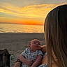 Larry is registered to the contest to win money with this photo: baby, woman, sunset, beach, ocean, sky, water, person, infant, holding, nature, outdoor, calm, scenic, relaxation, sunlight, clothing, portrait, warm, love
