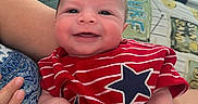 Larry joined the competition — help win amazing prizes! baby, smiling, infant, red_shirt, stars, striped_clothing, arm, hand, couch, quilt, fabric, person, indoor, portrait, happy, closeup, skin, head, face, child