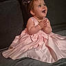 baby, child, pink_dress, clapping, couch, happy, smiling, indoor, portrait, cute, young_child, sitting, fabric, home, person, small_hands, joy, celebration, hairband, excitement