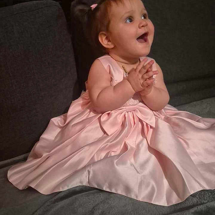 Alycia participe au concours pour gagner de l'argent avec cette photo : baby, child, pink_dress, clapping, couch, happy, smiling, indoor, portrait, cute, young_child, sitting, fabric, home, person, small_hands, joy, celebration, hairband, excitement