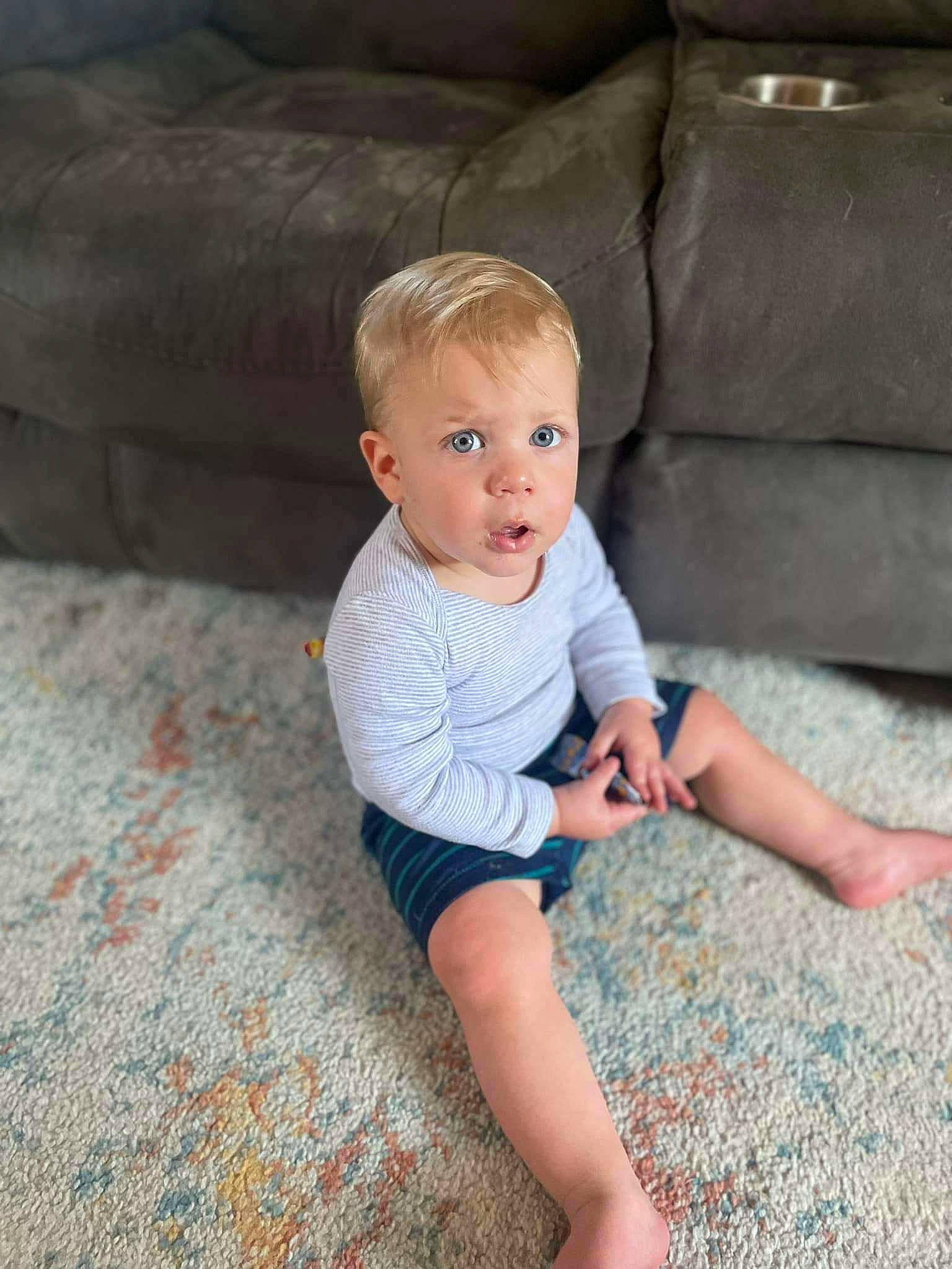 Jaxton is registered to the contest to win money with this photo: baby, baby_toddler_clothing, cheek, comfort, eye, face, floor, flooring, grass, hairstyle, head, human_body, knee, leg, person, shorts, skin, sleeve, surprise, t_shirt