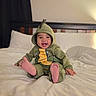 baby, child, dinosaur_costume, onesie, green_clothing, hood, smiling, laughing, sitting, bed, bedroom, pillow, blanket, bare_feet, toes, portrait, indoor, cozy, happy, photography