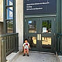 Azriel is registered to the contest to win money with this photo: child, toddler, mickey_mouse, tshirt, shorts, sandals, museum, door, sign, concrete, railing, reflection, glass, building, outdoor, daylight, person, shadow, parking, garden