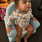 Azriel is registered to the contest to win money with this photo: toddler, child, pajamas, chair, plush_chair, christmas_tree, presents, holiday, indoor, carpet, curly_hair, cute, smiling, clothing, furniture, home, decorations, holiday_lights, person, sitting