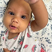 Nyla is registered to the contest to win money with this photo: baby, child, infant, face, hand, strawberry_pattern, shirt, blanket, floral, curious, wide_eyes, mouth_open, cute, close_up, skin, person, young, lying_down, indoors, portrait