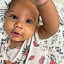 baby, child, infant, face, hand, strawberry_pattern, shirt, blanket, floral, curious, wide_eyes, mouth_open, cute, close_up, skin, person, young, lying_down, indoors, portrait