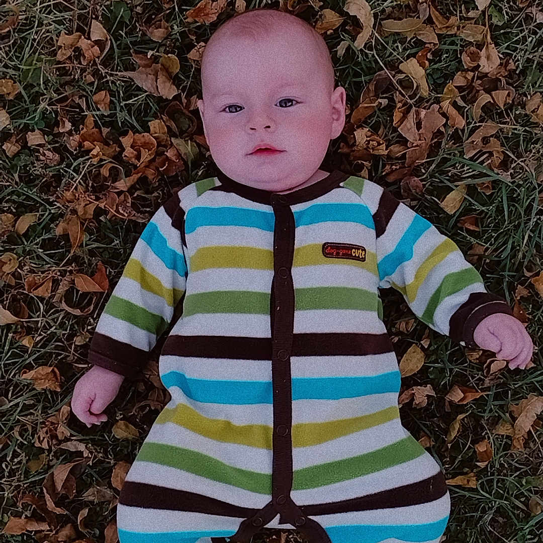 Jacob is registered to the contest to win money with this photo: baby, bodypart, clothing, coat, face, finger, footwear, grass, hand, head, jacket, knitwear, leaf, pants, person, photography, plant, portrait, shoe, sweater