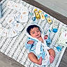 baby, infant, blue_robe, diapers, baby_wipes, baby_lotion, baby_oil, baby_powder, baby_brush, baby_scissors, baby_nail_clipper, baby_care, floor, rug, wood_floor, baby_bathrobe, cute, newborn, laying_down, indoors