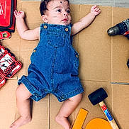 Thiago joined the competition — help win amazing prizes! baby, cardboard, casual_clothing, child, curly_hair, cute, denim_overalls, drill, expression, floor, indoor, infant, lying_down, person, playful, portrait, rubber_mallet, toolkit, tools, wood_floor
