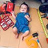 Thiago is registered to the contest to win money with this photo: baby, cardboard, child, construction, cute, denim_overalls, drill, face_paint, floor, foam_number, hammer, indoor, infant, playful, red_tool_bag, screwdriver_set, tape_measure, tools, wheel, wood_floor