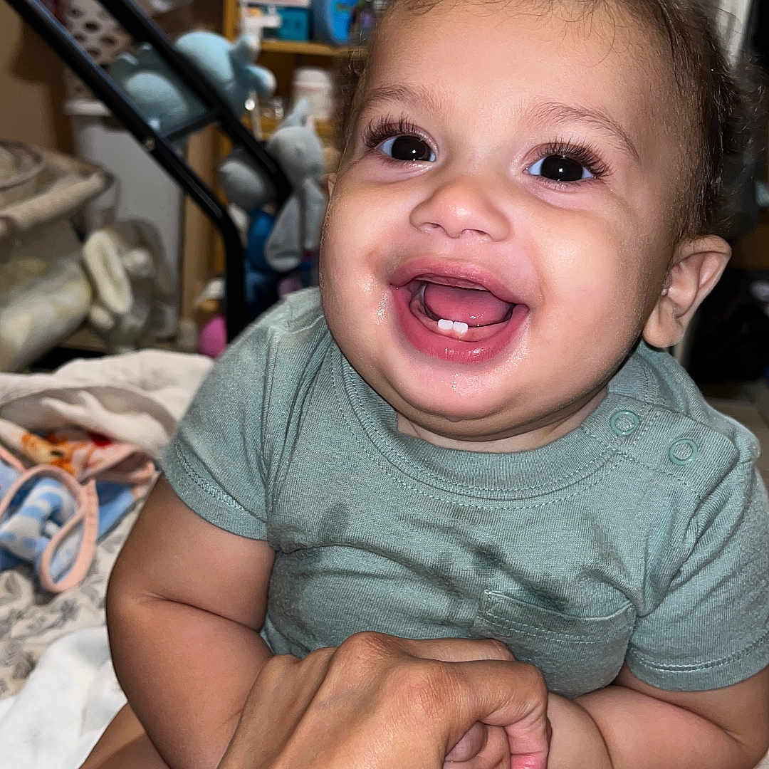 Argenis is registered to the contest to win money with this photo: baby, smiling, hand, infant, indoor, clothing, person, cute, child, furniture, shelf, toy, happy, face, eyes, skin, holding, room, baby_girl, expression