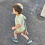 child, running, pacifier, blanket, shorts, tshirt, sneakers, outdoor, pavement, sunlight, shadow, concrete_wall, casual_clothing, active, motion, daylight, young_child, boy, side_view, playful